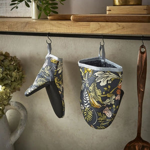Two Ulster Weavers Finch & Flower Cotton Microwave Mitts hang from black hooks on a kitchen wall rod, with a wooden spoon and kitchen decor in the background.