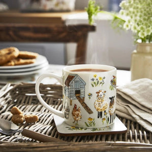 Mug with farm animal design on a table with a plate of pastries and a vase of flowers.