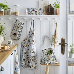 Kitchen scene with aprons, oven mitts, and a bag hanging on a white wall from the Ulster Weavers Portman Farm collection.