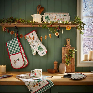Decorative kitchen scene with Christmas stockings, oven mitts, and a mug on a wooden counter from the Ulster Weavers Winter Walkies collection.