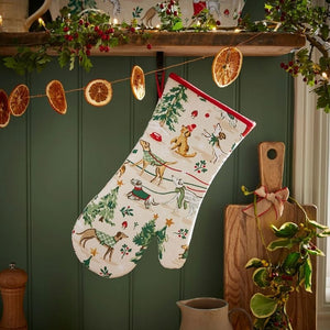 Ulster Weavers Winter Walkies Oven Mitt  hanging on a green wall with dried oranges and a wooden shelf.