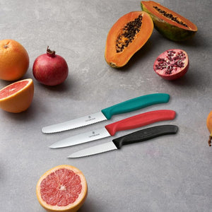 Victorinox Swiss Classic Paring Knife Set with black, red and turquoise handles shown with fruit on a grey surface.