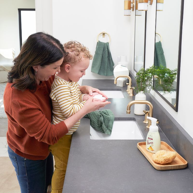 Woman and child washing hands in a modern bathroom with a bottle of Young Living Thieves foaming hand soap on a tray.