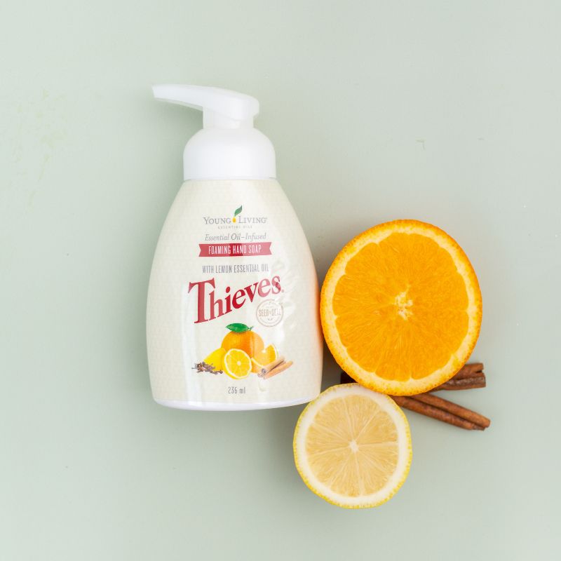 Young Living Thieves hand soap bottle with an orange, lemon, and cinnamon stick on a light green background