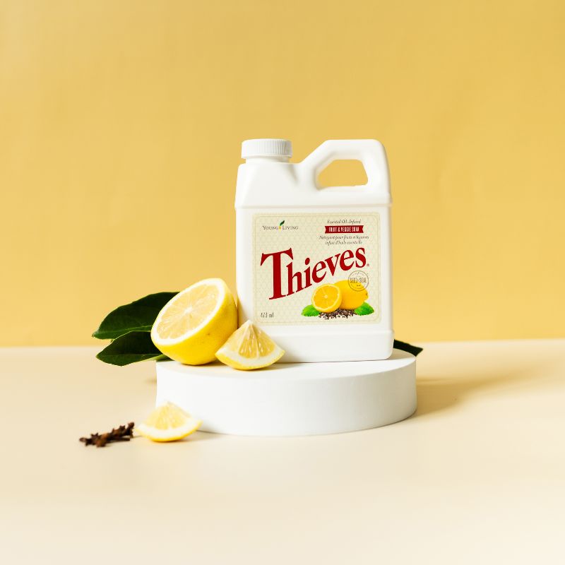Young Living Thieves Fruit & Veggie Wash with lemons and cloves on a yellow background