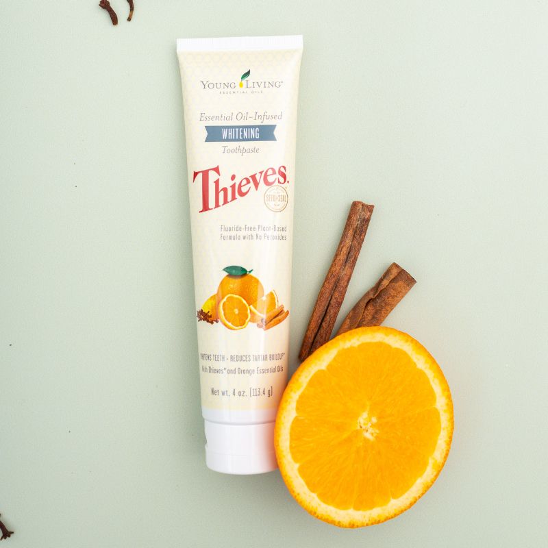 Young Living Thieves Whitening Toothpaste tube with an orange and cinnamon sticks on a light green background