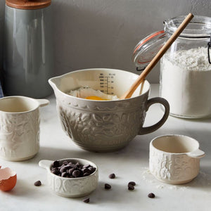 Mason Cash In The Forest Measuring Jug shown alongside measuring cups, flour, eggs and chocolate chips.